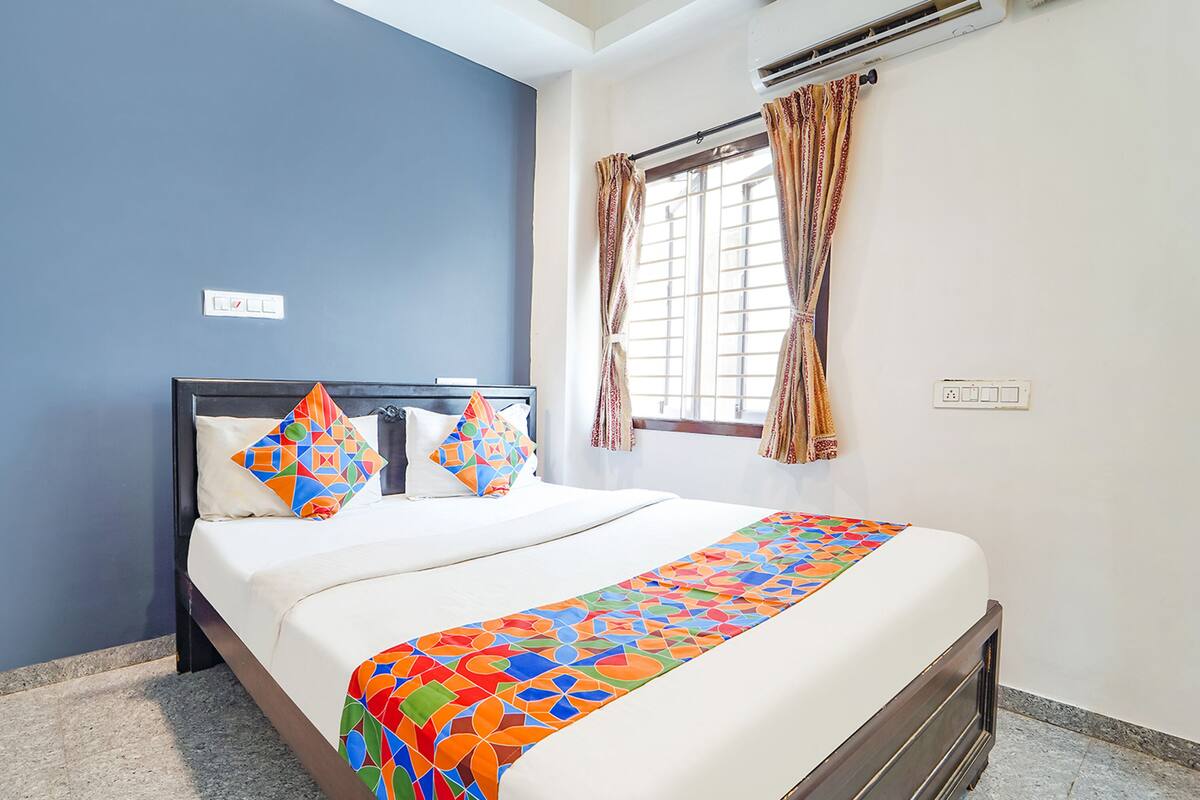 Cama bem arrumada com colcha geométrica colorida, cabeceira escura e duas almofadas decorativas.