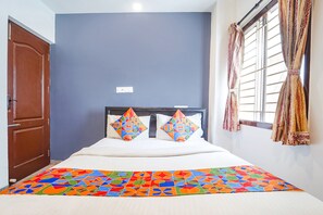 A bedroom with a bed, two pillows, a colorful bedspread, a wooden door, and a window with curtains. - FabExpress Global Stay (Coimbatore)