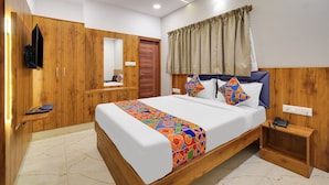 A bedroom with a bed, wooden wardrobe, a bedside table, a ceiling fan, and a window with curtains. - FabHotel Royal Grand (Bengaluru)