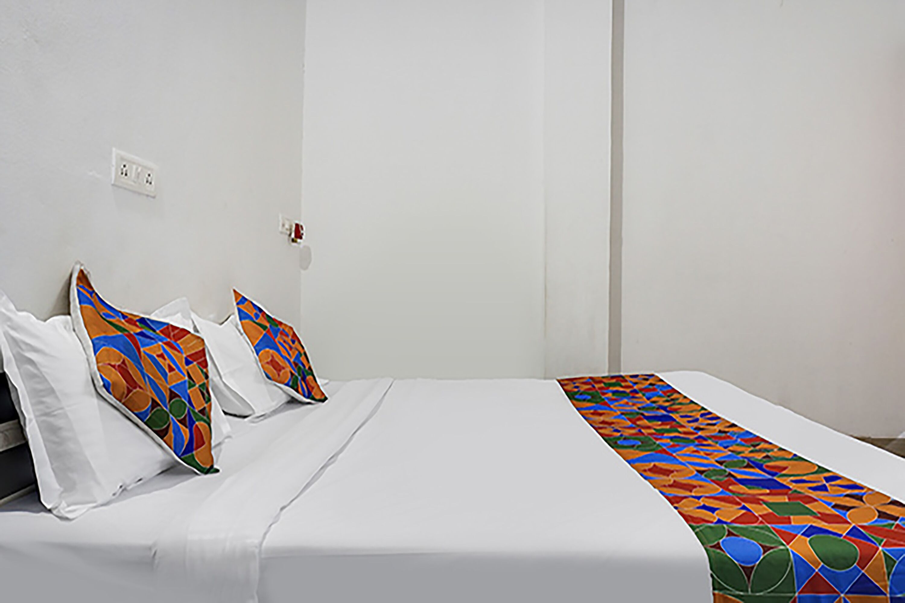 A neatly made bed with white linens and colorful geometric-patterned pillows.