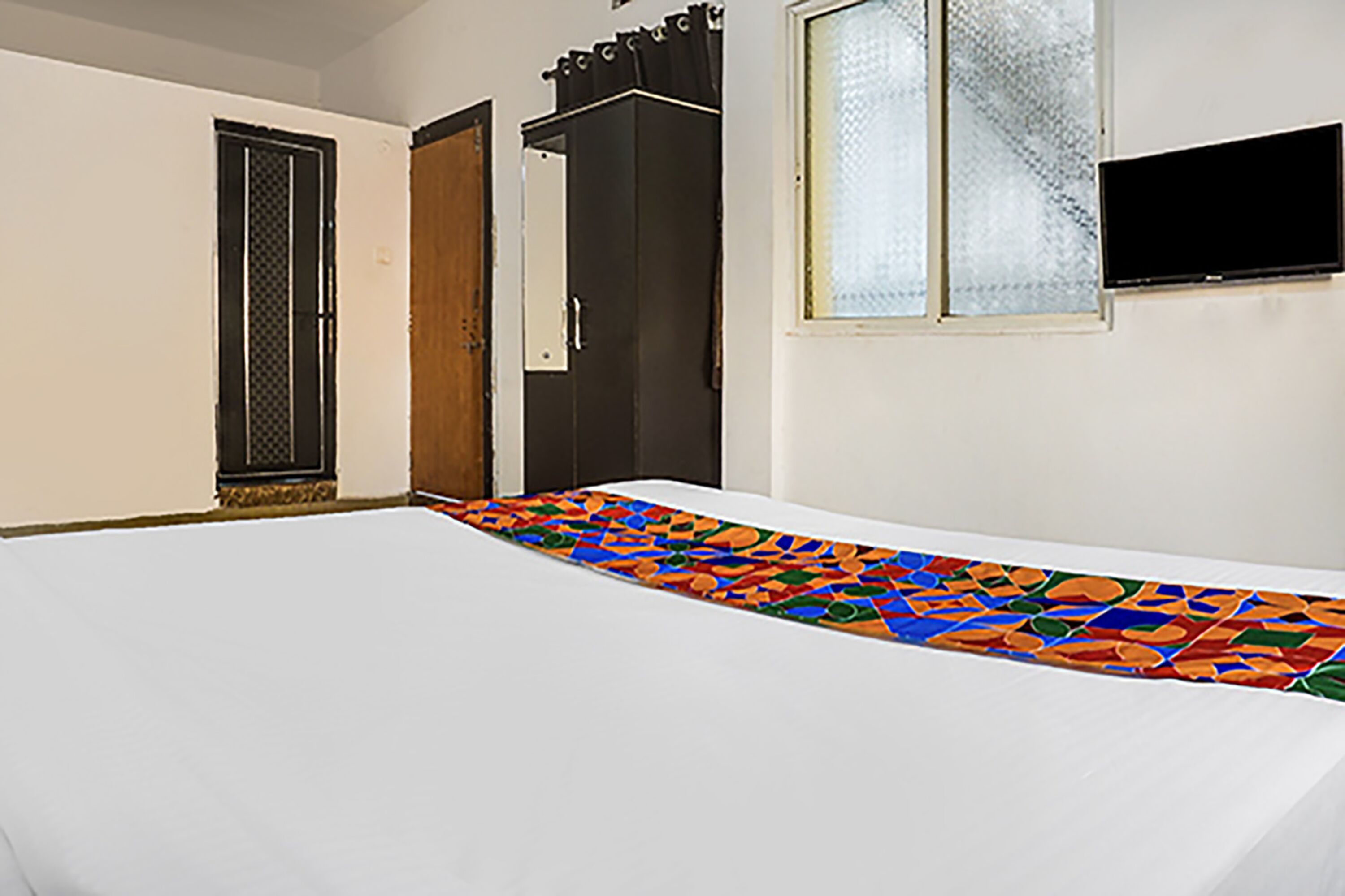 A room with a bed, a wardrobe, a television mounted on the wall, and a window with frosted glass.