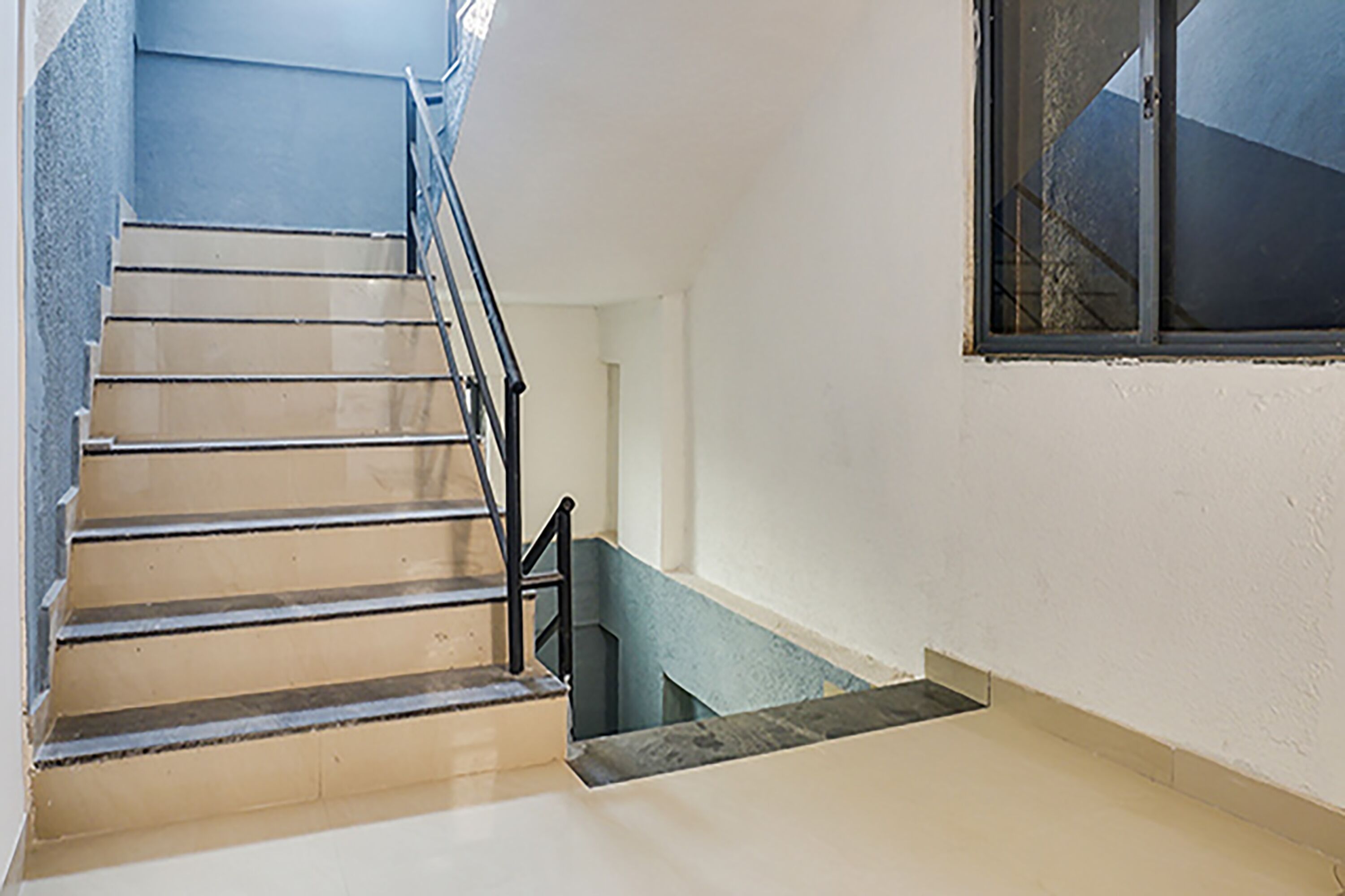 Una escalera con peldaños color beige y barandillas negras, que conduce a un rellano con un ventanal.
