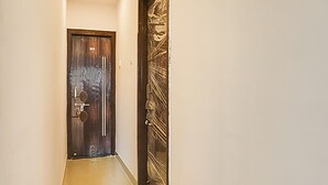 A hallway with a wooden door, a metal handle, and a small round mirror on the wall. - FabHotel Galaxy Airport Inn (Pune)