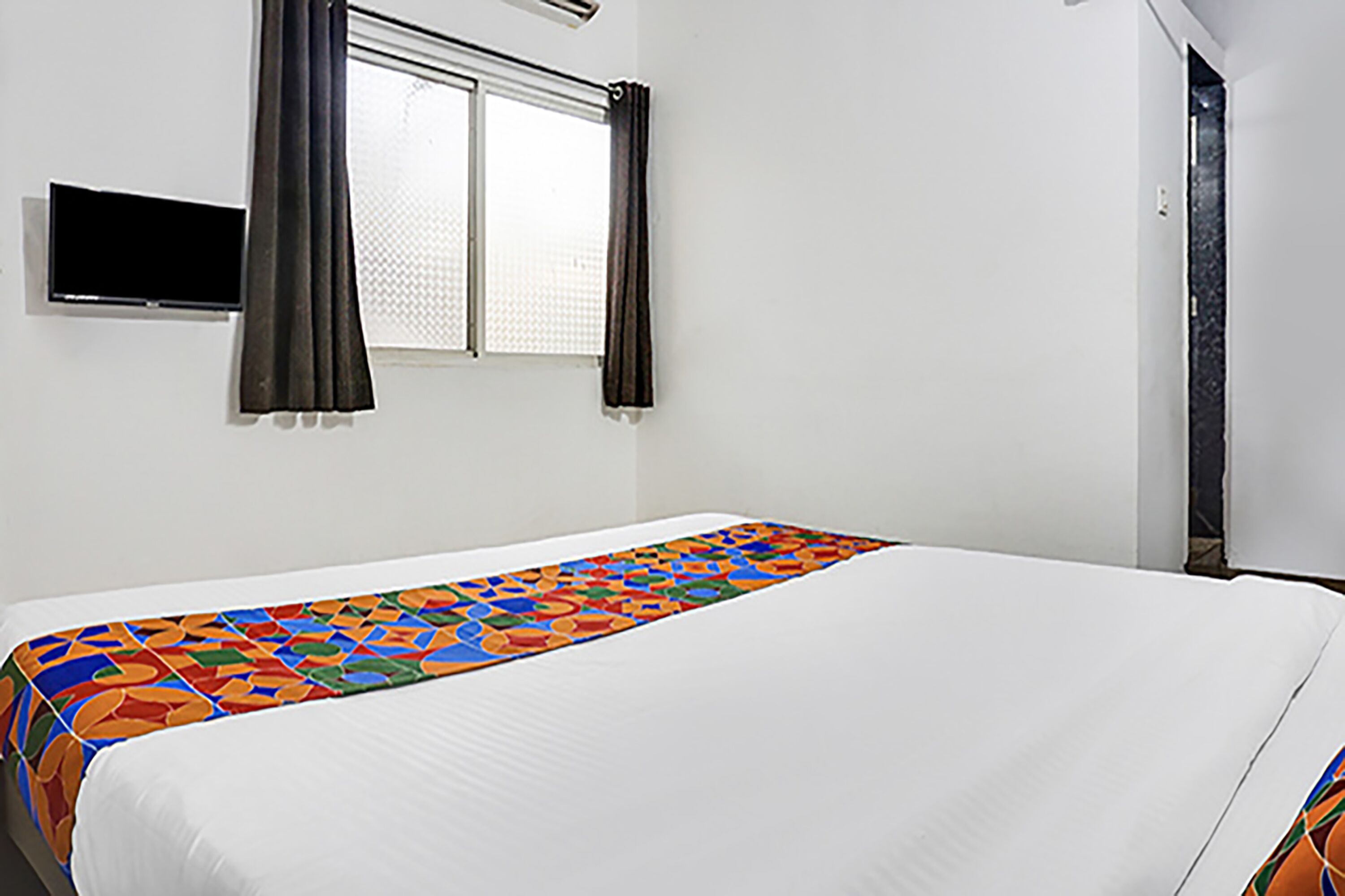 A hotel room with a bed, a television mounted on the wall, and a window with curtains.