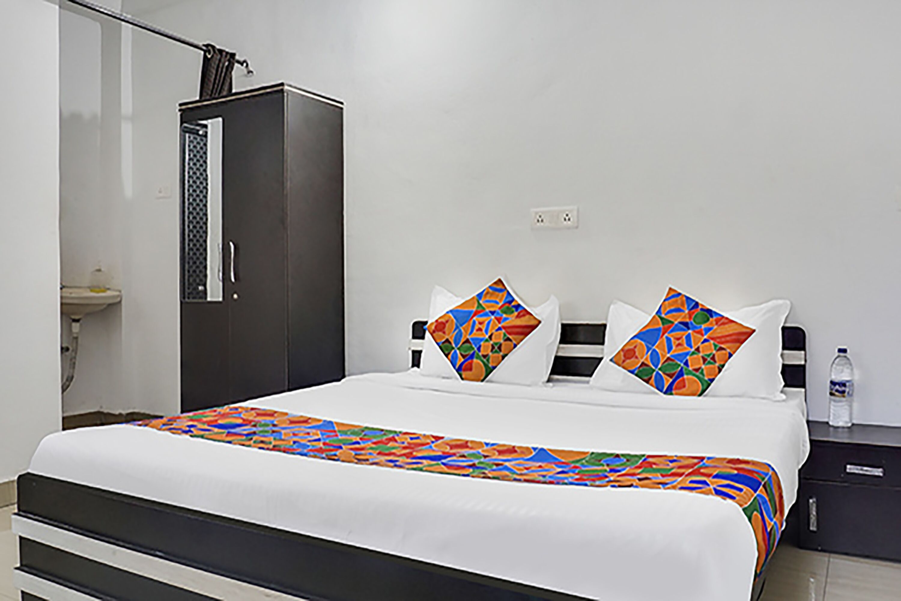 A hotel room with a bed, a wardrobe, and a nightstand with a bottle.