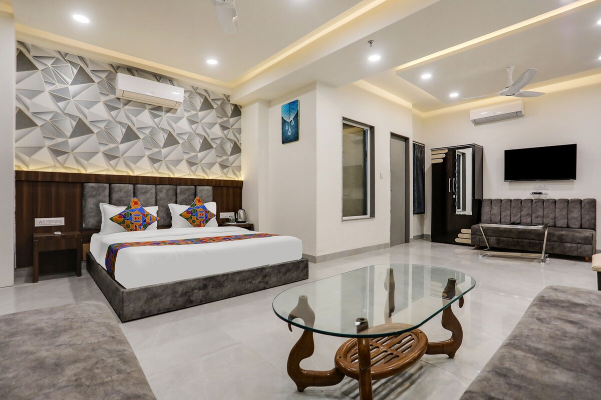 A modern hotel room with a large bed, a glass coffee table, a sofa, and a flat-screen TV.