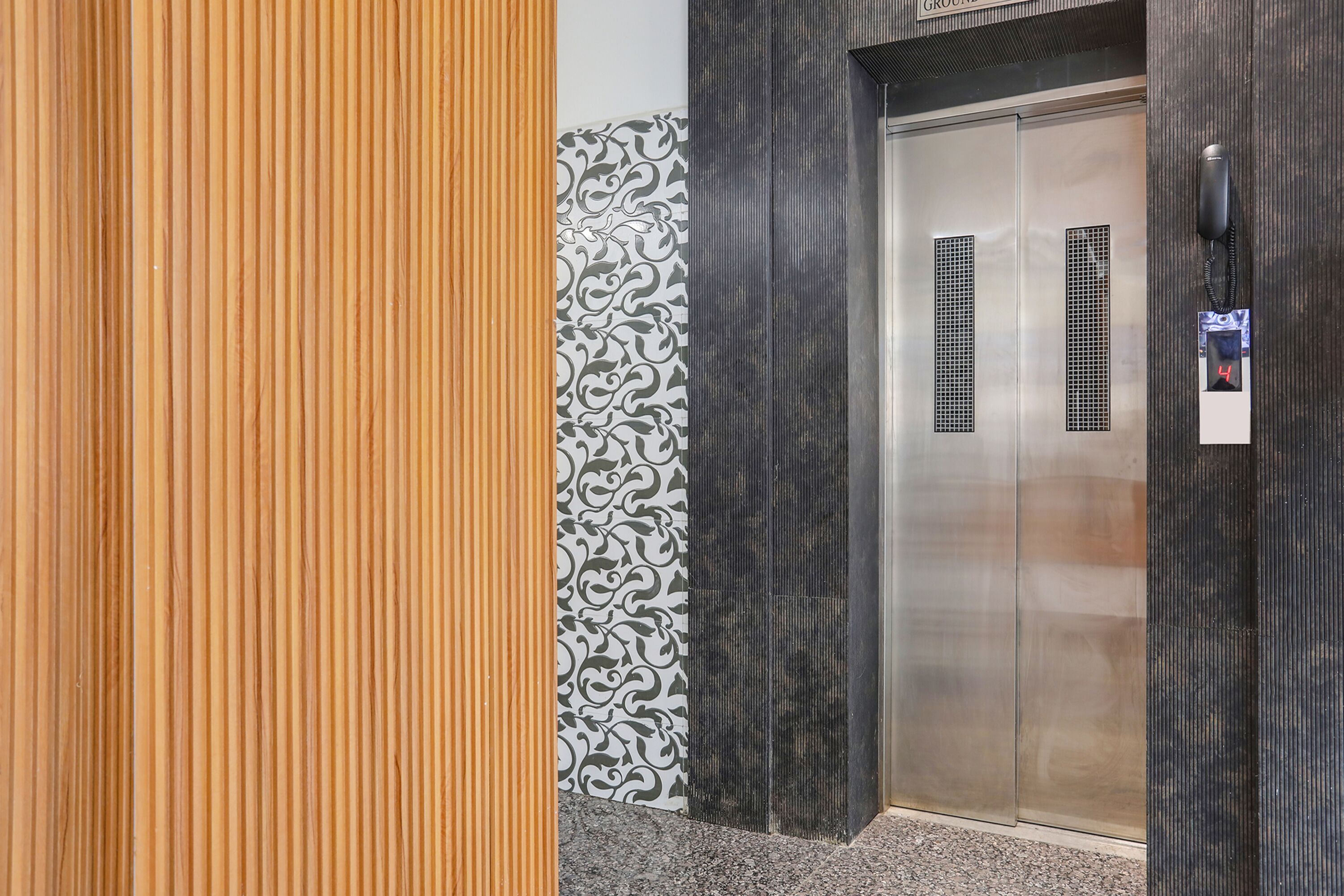 An elevator with a metallic finish, a patterned wall, and a wooden panel.