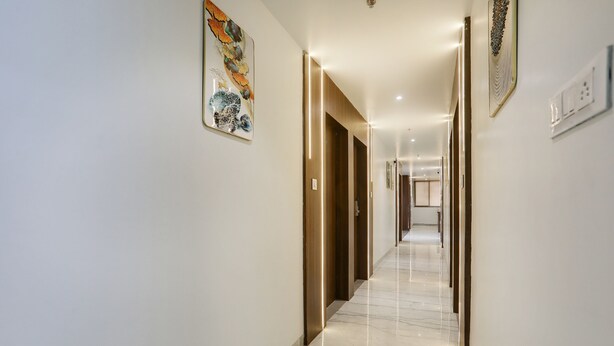Un couloir d’hôtel moderne avec un sol en marbre, des portes en bois et des œuvres d’art accrochées aux murs.