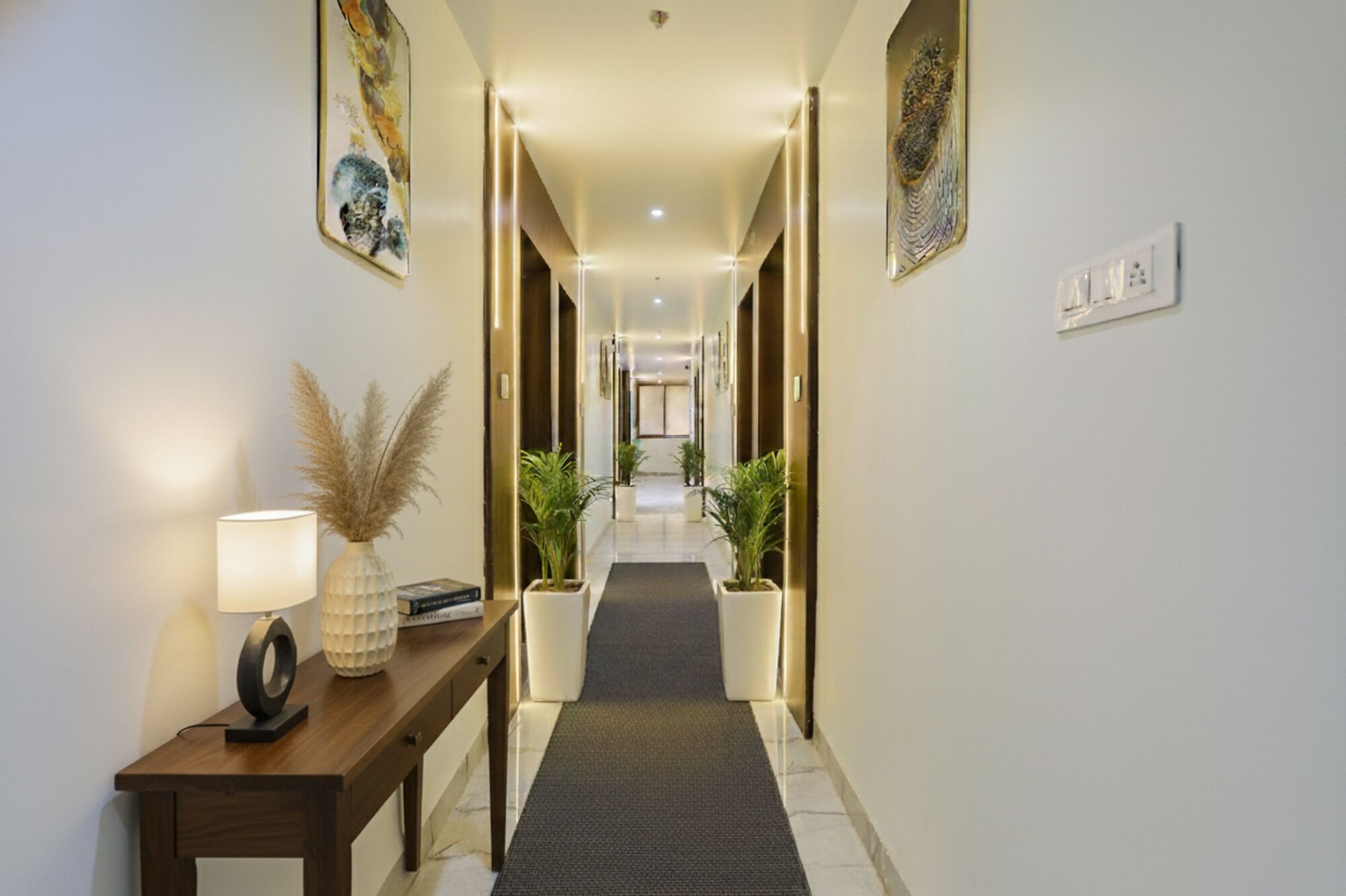 A hallway with a wooden console table, a lamp, and potted plants.