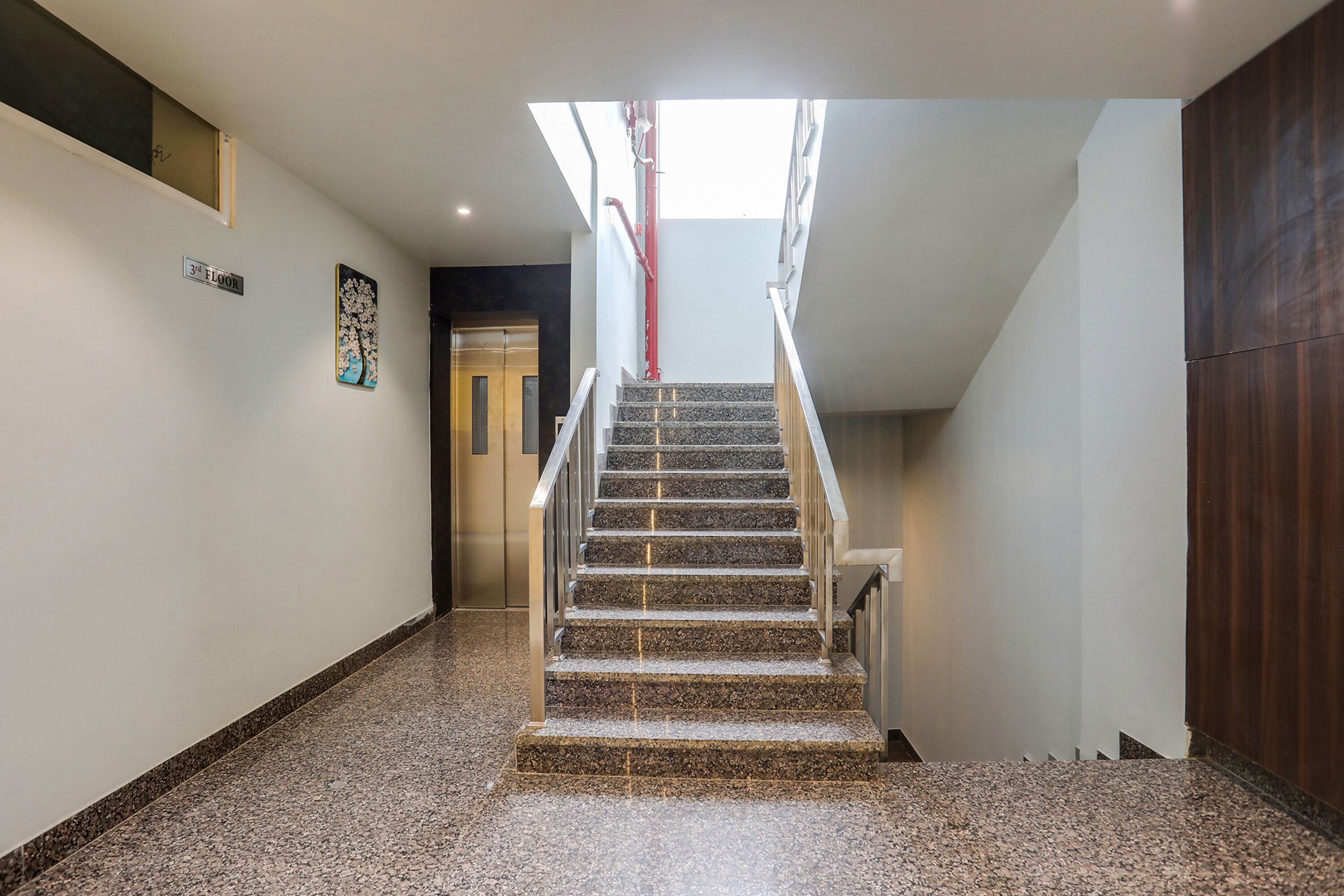 A staircase leading to a second floor with a handrail, a door at the end, and a wall-mounted sign indicating the floor level.