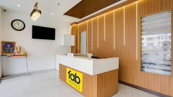 A reception desk with a wooden finish and a 'fab hotels' logo. There is a wall-mounted clock and a flat-screen TV above the desk.