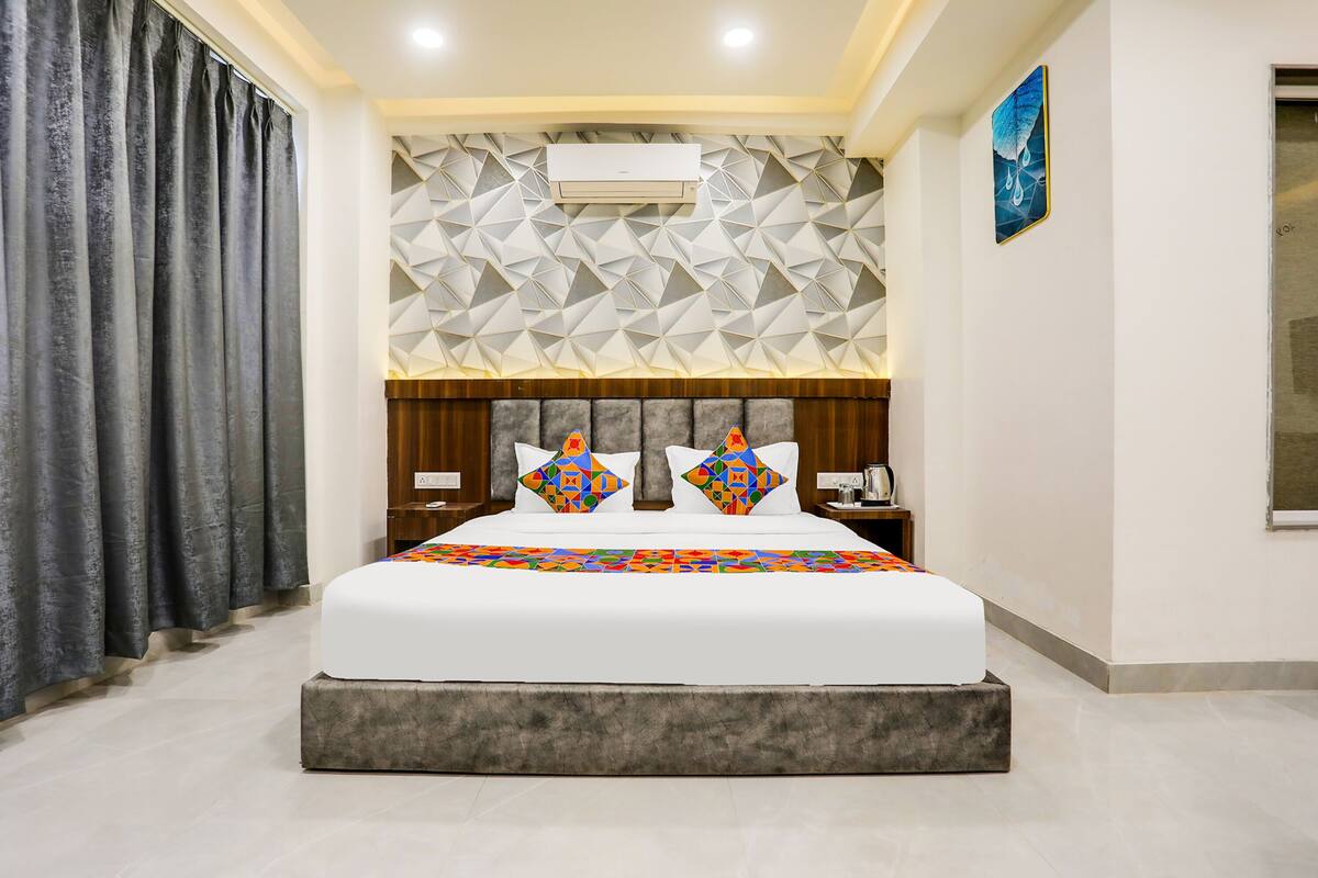 A modern hotel room with a large bed, geometric patterned wall, air conditioning unit, and a painting on the wall.