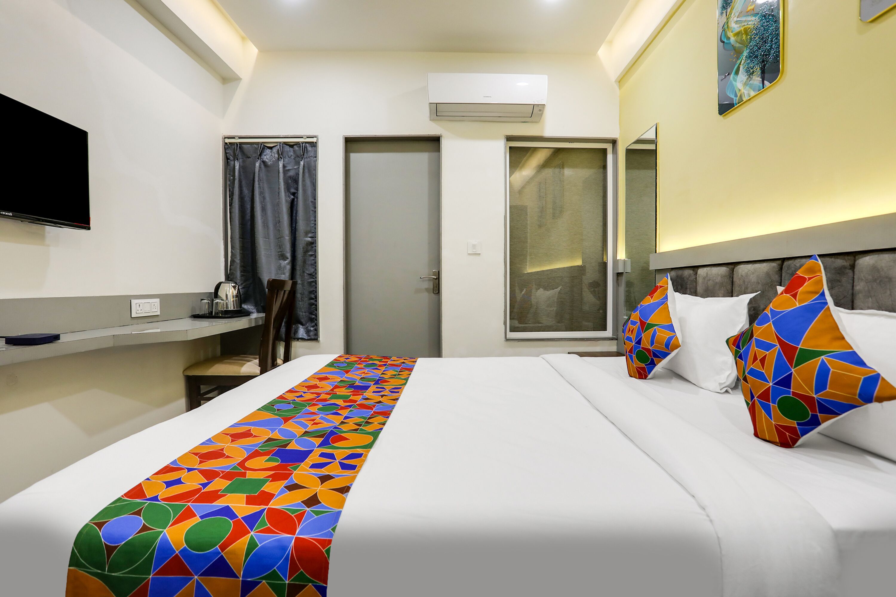 Una habitación de hotel con una cama, televisión, escritorio y ventana con cortinas.