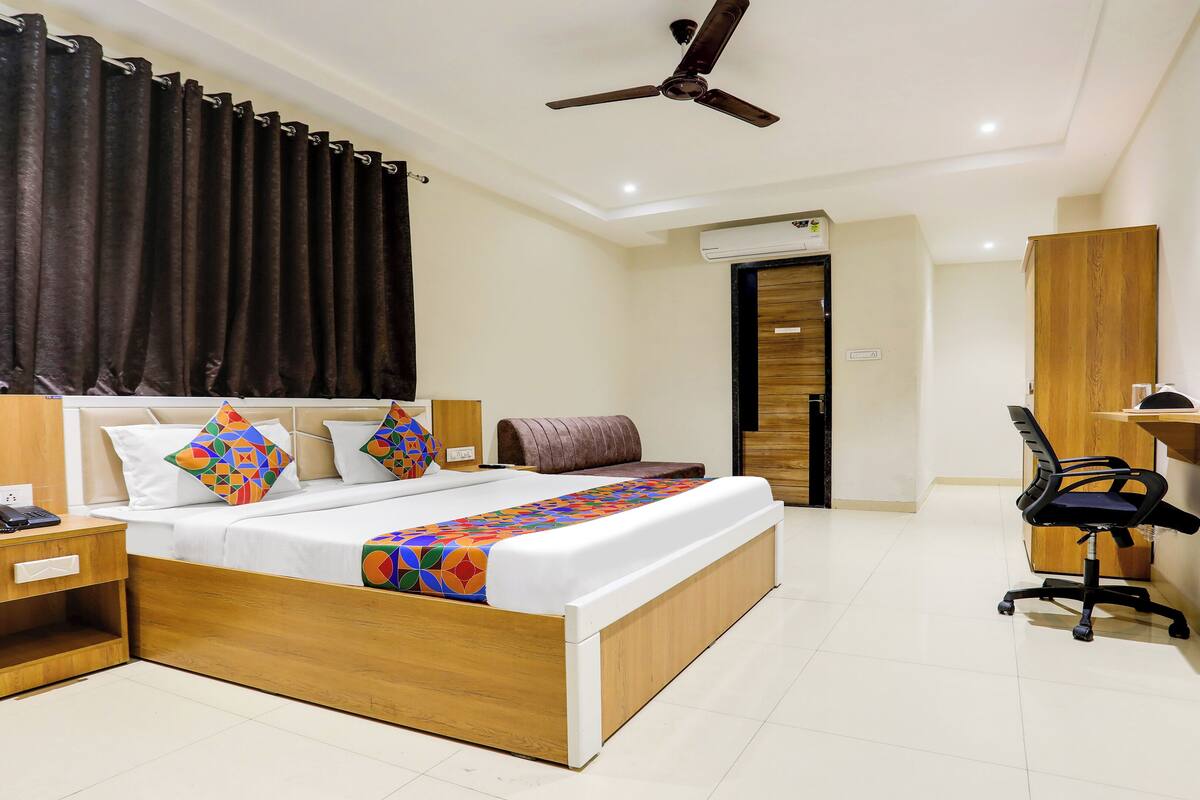 Une chambre d’hôtel comprenant un lit, une table de chevet, un bureau avec une chaise, un ventilateur de plafond et un appareil de climatisation.