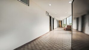 A hallway with patterned flooring, a brown sofa, and a potted plant. - FabHotel Mansarovar Inn (Raipur)