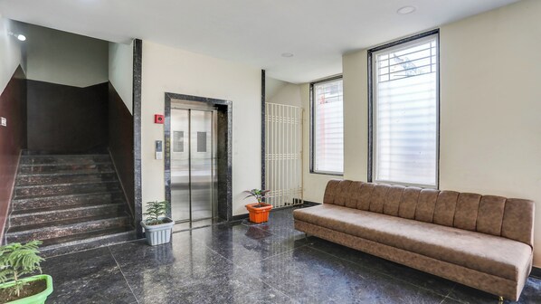 A lobby with a staircase, elevator, potted plants, a sofa, and large windows.