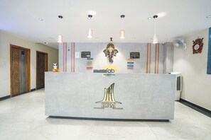 A reception desk with a logo, a clock, and a fan on the wall. - FabHotel Park Mahindra (Raipur)