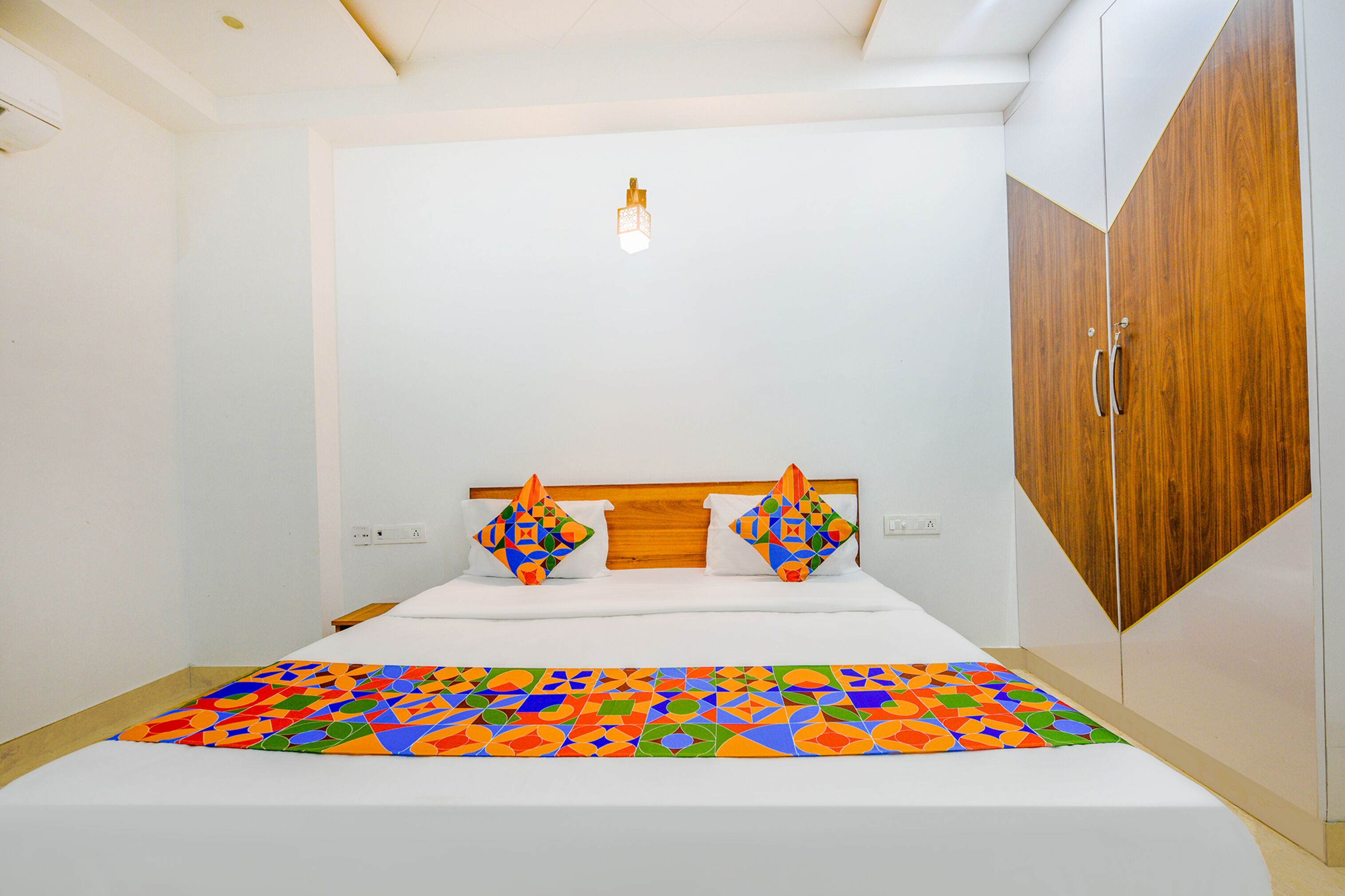 A bedroom with a bed, a wooden wardrobe, and a colorful geometric-patterned bedspread.