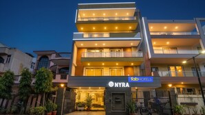 A multi-story hotel with a modern design, featuring balconies on each floor and a well-lit entrance. - FabHotel Nyra Residency (Gurugram)