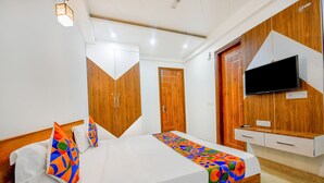 A hotel room with a bed, wooden wardrobe, a TV mounted on the wall, and a small desk with drawers. - FabHotel Nyra Residency (Gurugram)