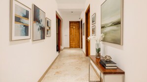 A hallway with framed abstract paintings, a wooden door at the end, and a console table with books and a vase of flowers. - FabHotel Nyra Residency (Gurugram)