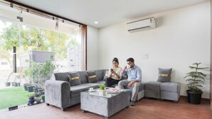 A modern living room with a grey sectional sofa, a glass coffee table, and a potted plant. - FabHotel Sky - Nr. Sapphire 83 Mall, Manesar (Gurugram)