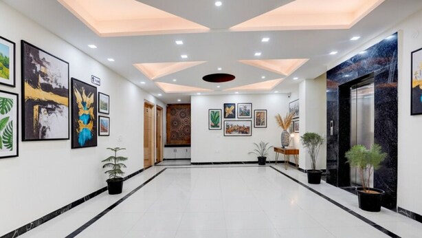 A spacious hallway with a modern ceiling design, framed artwork on the walls, and potted plants. - FabHotel Sky - Nr. Sapphire 83 Mall, Manesar (Gurugram)