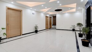 A spacious, well-lit hallway with a tiled floor, wooden doors, and potted plants. - FabHotel Sky - Nr. Sapphire 83 Mall, Manesar (Gurugram)