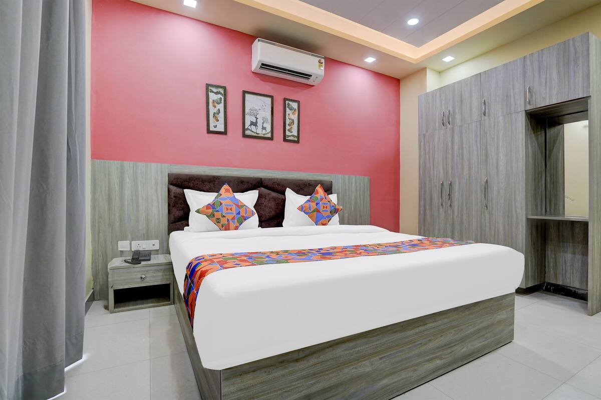 A modern bedroom with a large bed, a nightstand, a wardrobe, and an air conditioning unit on the wall.