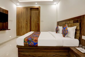 A neatly arranged hotel room with a wooden headboard, a bed with a colorful geometric bedspread, two white pillows, and a wooden bedside table with glasses and a tray.