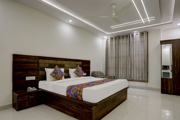 A modern bedroom with a wooden headboard, a bed with patterned pillows, a bedside phone, and a ceiling fan.