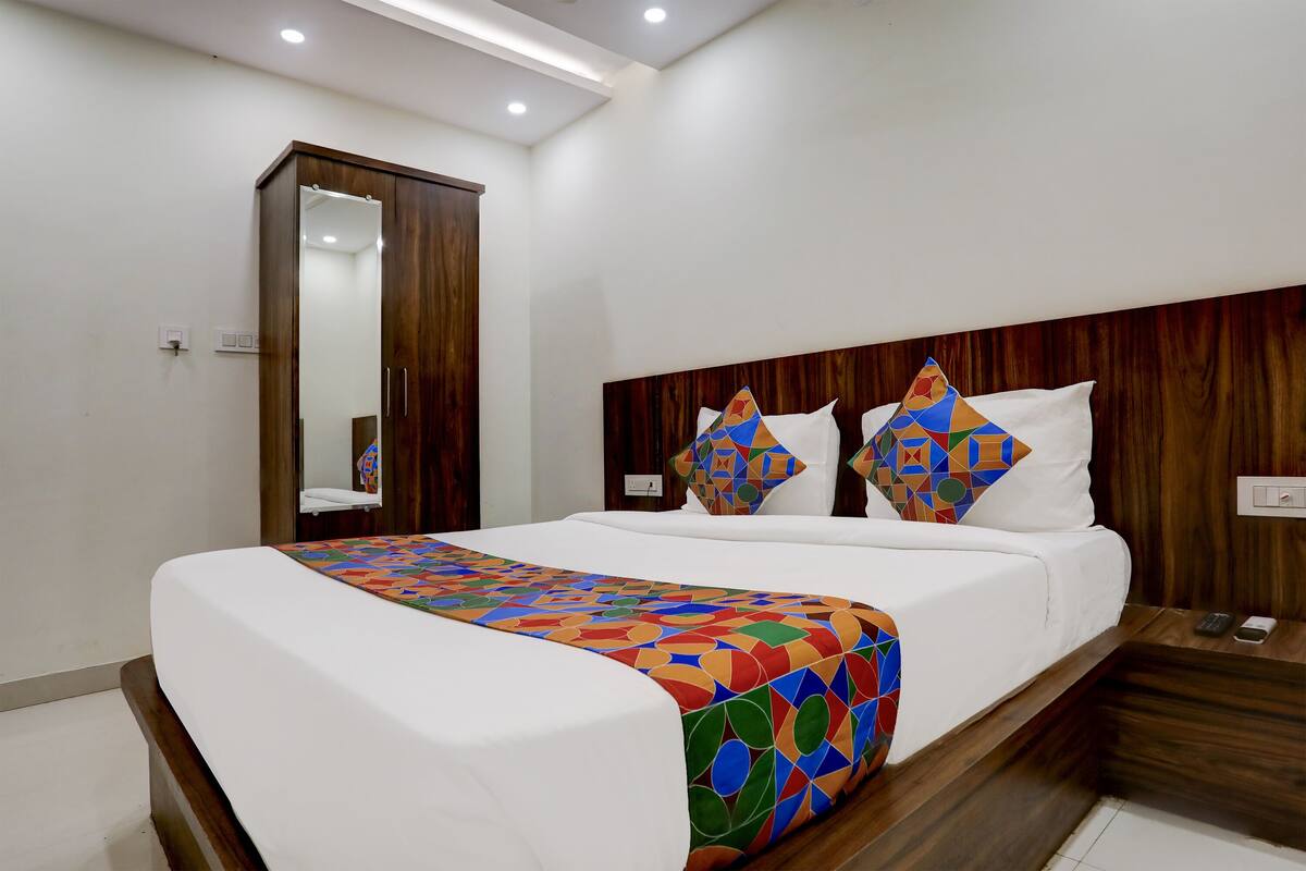 A neatly made bed with a colorful quilt, a wooden headboard, and a mirror on the wall.