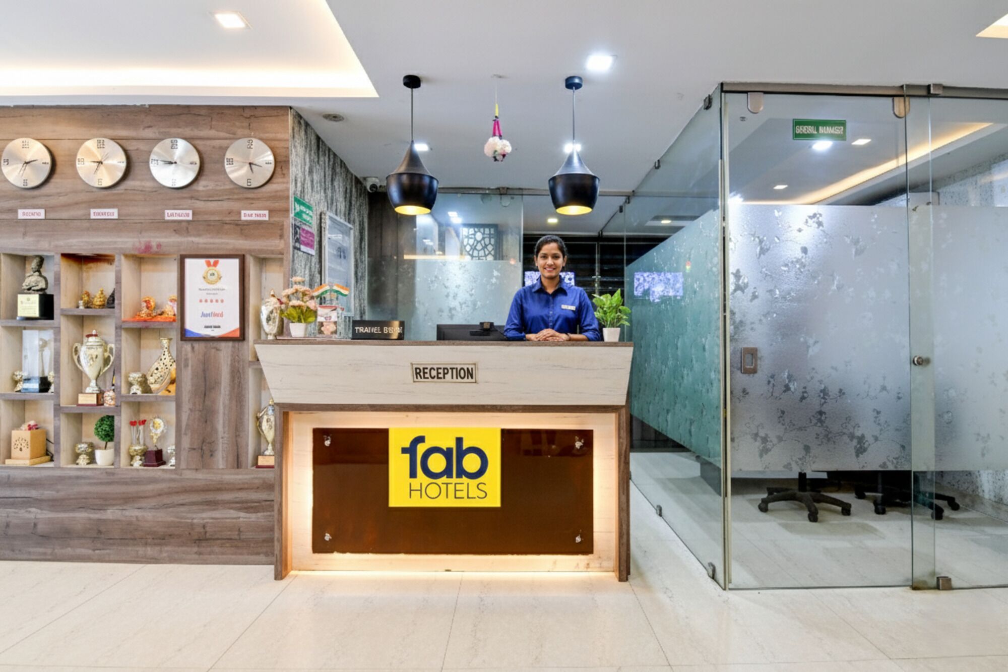 A reception desk with a sign for Fab Hotels, a wall with clocks, and a glass door to the right.
