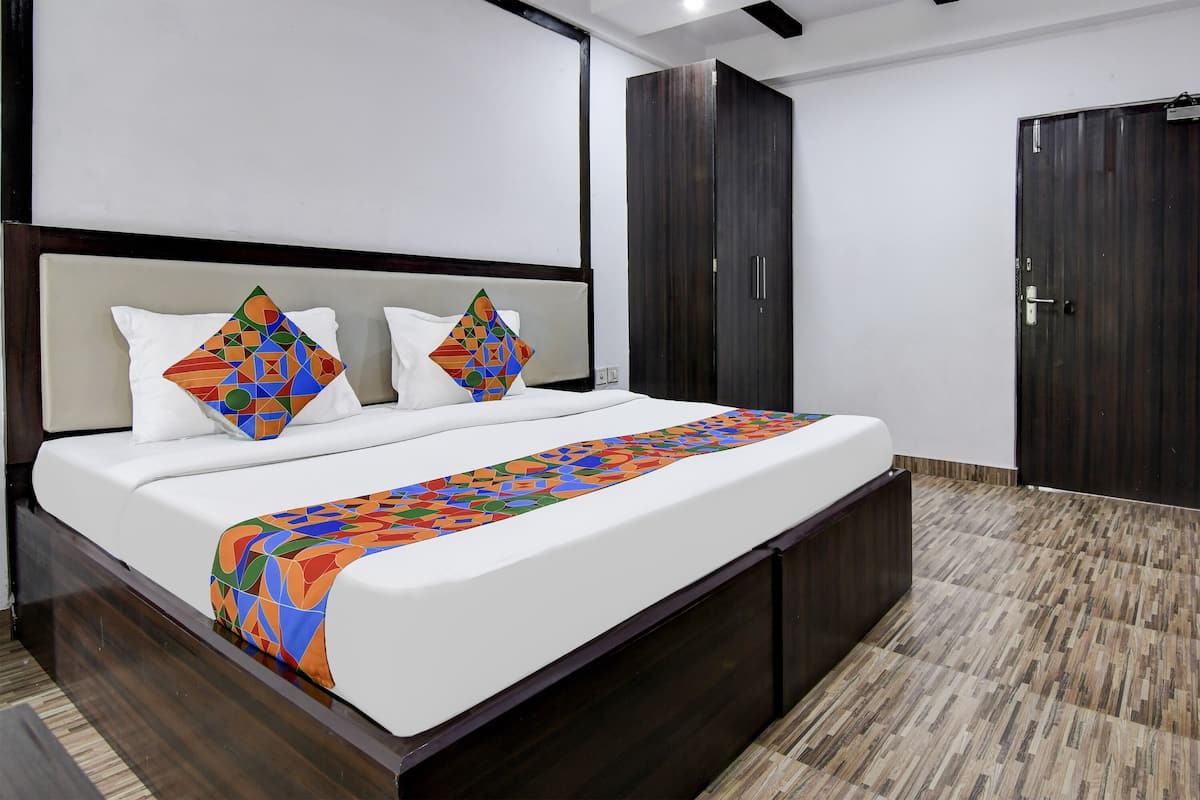 A modern hotel room with a large bed, dark wooden wardrobe, and a patterned bedspread.