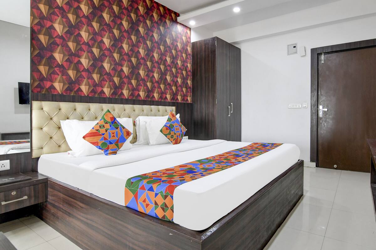 A modern hotel room with a large bed, a headboard with a geometric pattern, a wooden wardrobe, and a door with a handle.