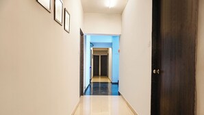Ein Flur mit einer dunklen Holztür rechts, einer blauen Wand und einem gefliesten Boden.