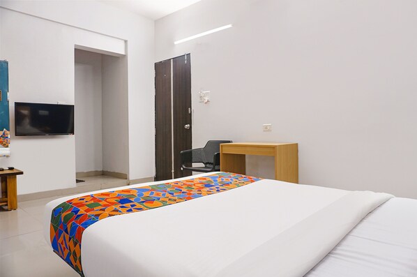 Una habitación de hotel con cama, escritorio, silla, televisor y puerta.