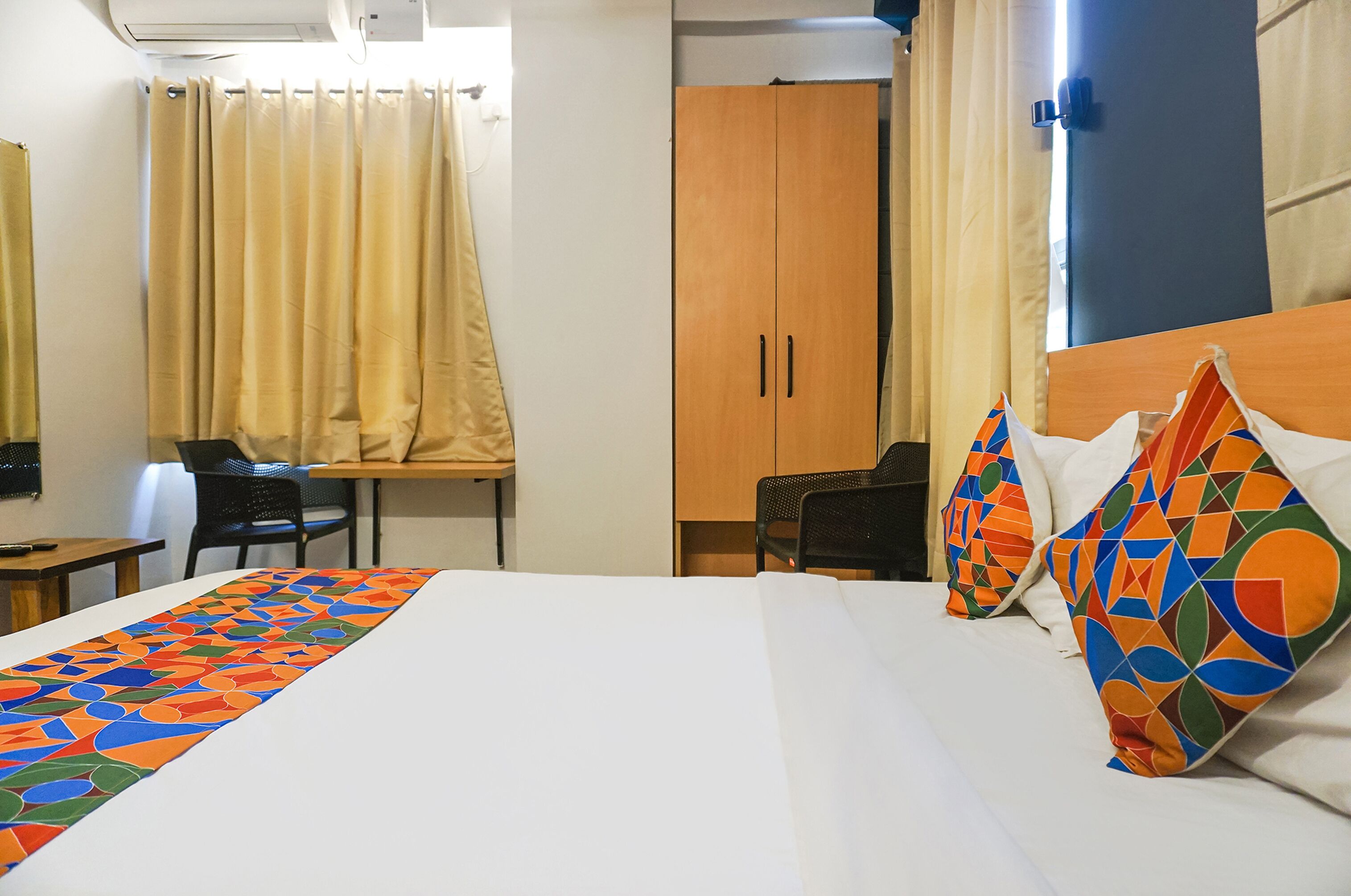 A hotel room with a bed, a desk, a chair, a wardrobe, and a window with curtains.