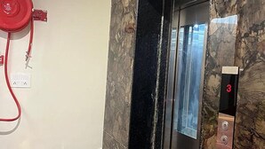 Un ascensor con pared de mármol, manguera contra incendios roja y teléfono de emergencia a la vista.