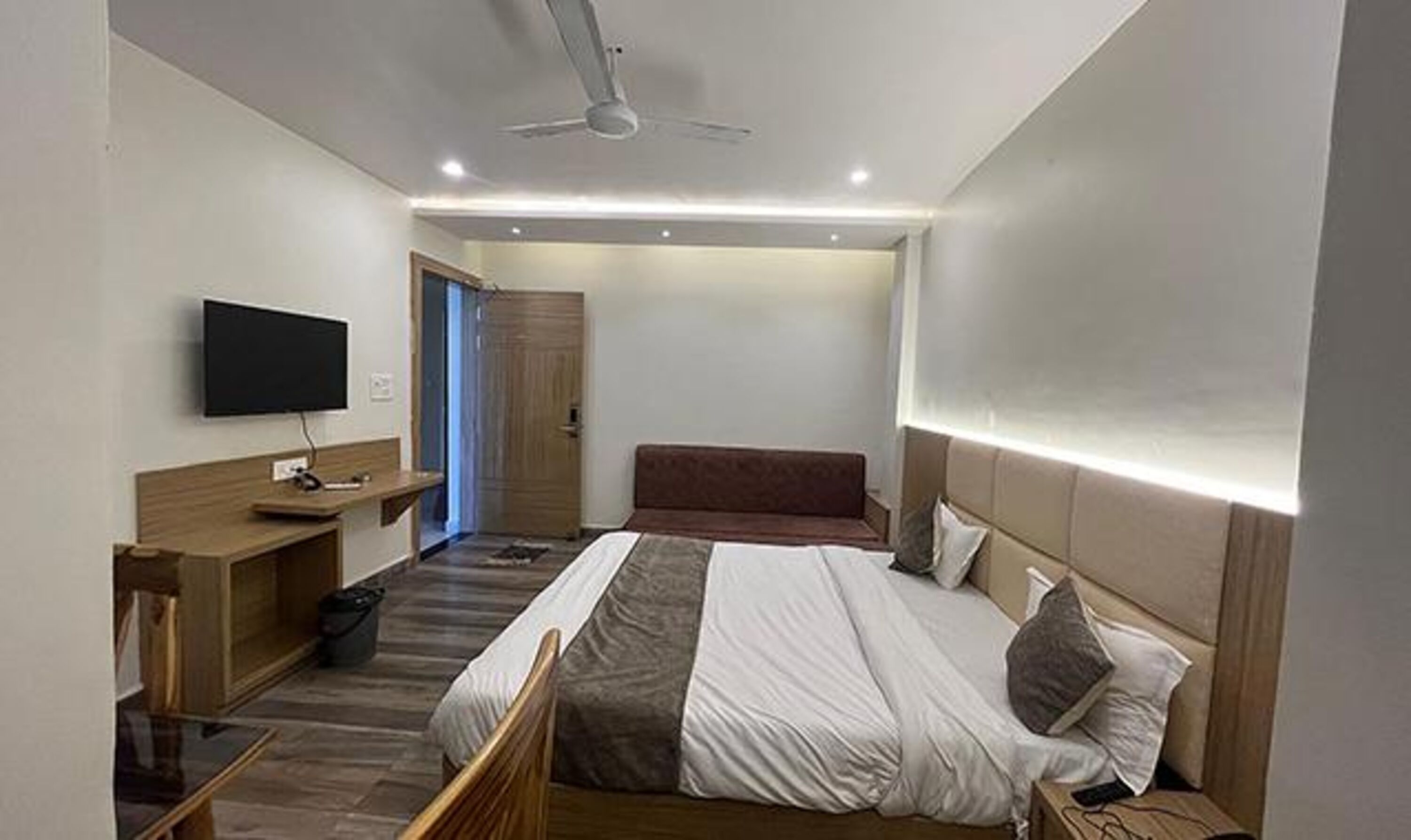 Ein modernes Hotelzimmer mit Bett, Fernseher, Schreibtisch und Deckenventilator.