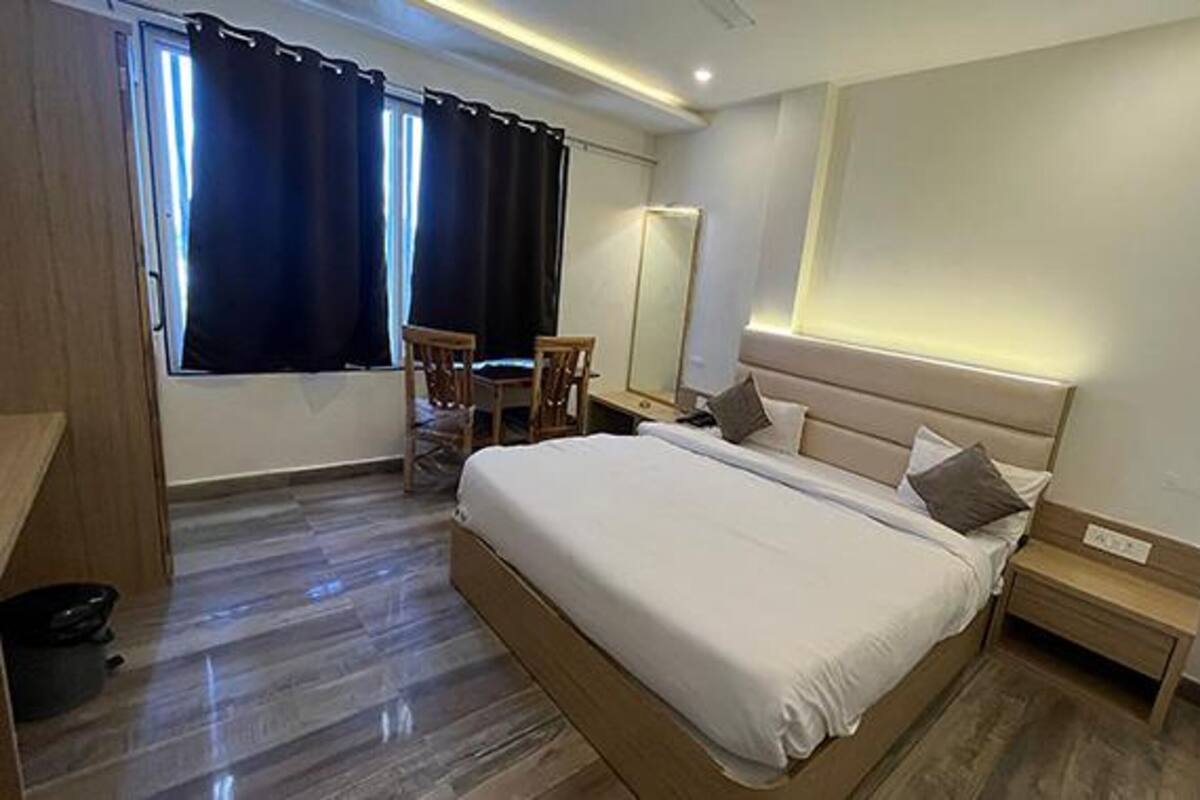 A hotel room with a large bed, a desk, a chair, and a window with curtains.