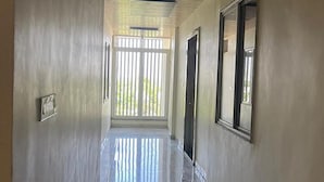 Un pasillo con una puerta al final, una ventana con persianas verticales y una lámpara en el techo.