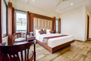 A hotel room with a large bed, a wooden headboard, a desk with a chair, and a window with curtains.