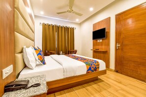 A hotel room with a bed, a television mounted on the wall, a wooden door, and a ceiling fan.