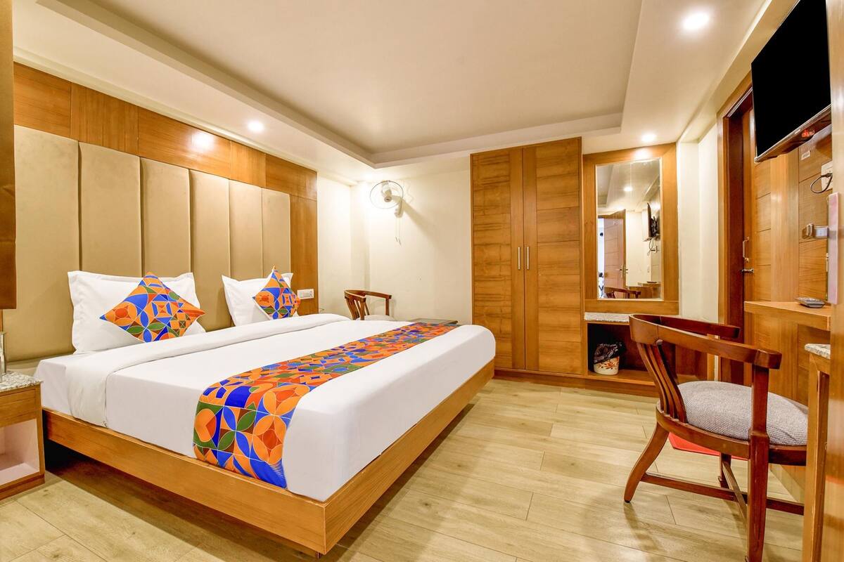 A bedroom with a large bed, wooden headboard, a bedside table, a chair, a TV, and a wardrobe.