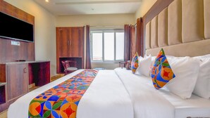 Ein Hotelzimmer mit einem großen Bett, einem an der Wand montierten Fernseher, Holzschränken und einem Fenster mit Vorhängen.