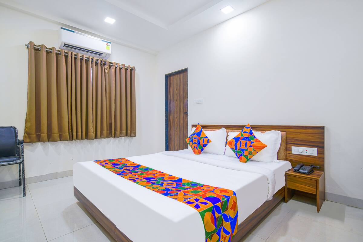 Una habitación de hotel con una cama grande, una mesita de noche con teléfono y un equipo de aire acondicionado en la pared.