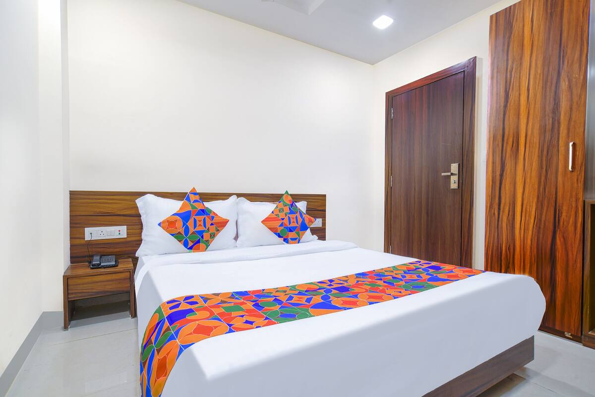 Una cama bien hecha con un edredón de estampado geométrico y colores vivos, un cabecero de madera y una mesita de noche con un teléfono.