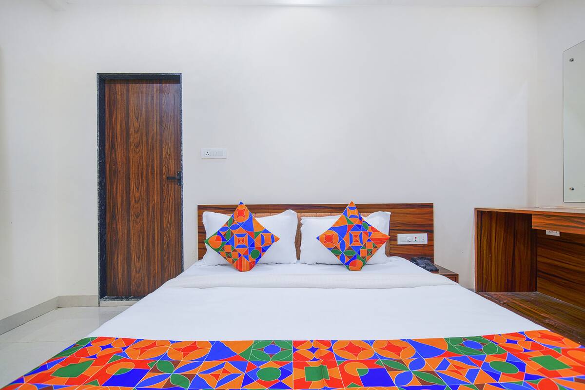 Una cama bien hecha con un edredón de estampado geométrico y colores vivos, dos almohadones decorativos y un cabecero de madera.