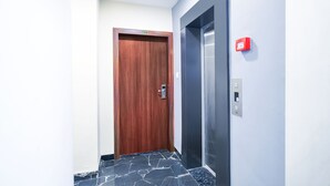 Corridoio con una porta in legno con il numero 208, un ascensore e una cassetta rossa di emergenza.